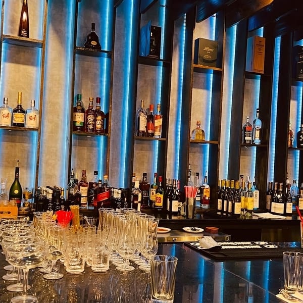 A well-stocked bar with various liquor bottles on shelves illuminated by blue LED lights.