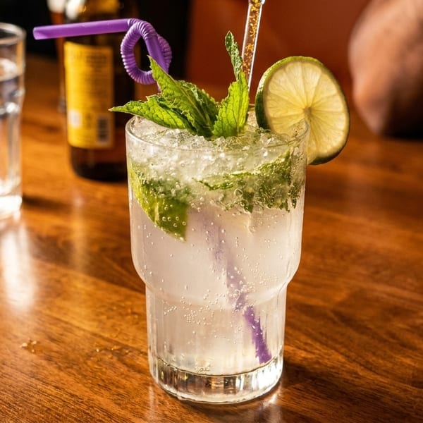 A refreshing mojito with mint and lime, next to a glass of water on a wooden table.