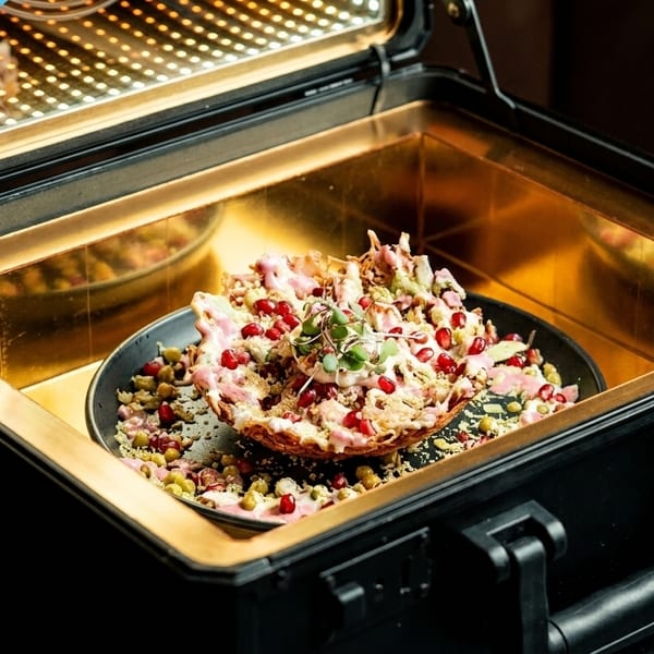 A colorful dish with pomegranate seeds and microgreens, served in a black case with a golden interior.