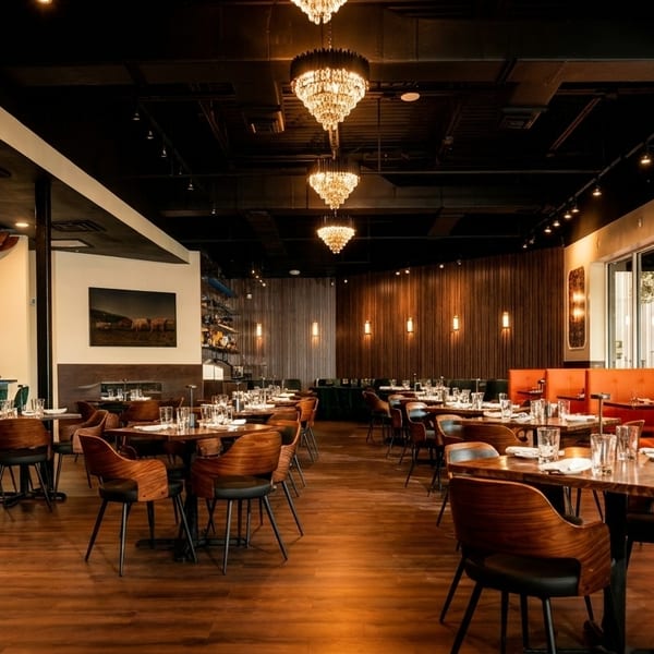 Spacious restaurant interior with dark wood floors, modern tables, orange booths, and a long bar with teal stools.