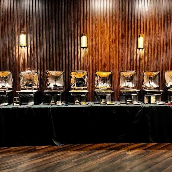 A buffet line with multiple chafing dishes and a fruit platter against a wooden wall.